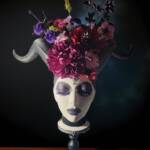 A painted styrofoam head with maleficent horms and a bouruwt of dark coloured flowers coming out of the top of her head.