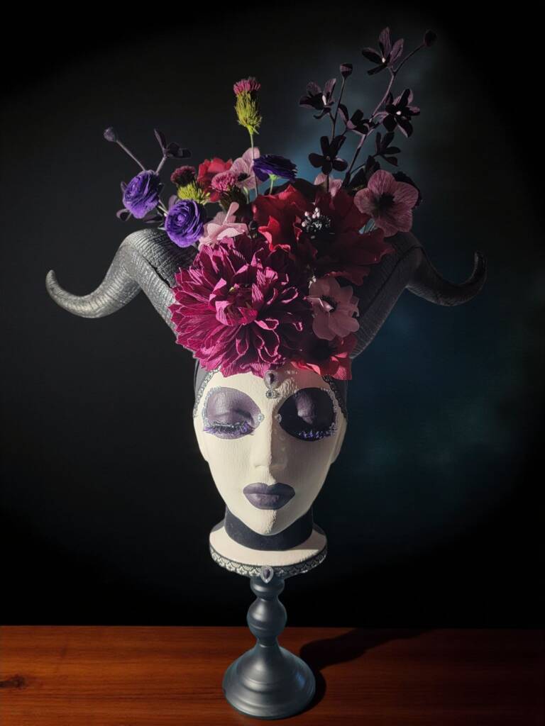 A painted styrofoam head with maleficent horms and a bouruwt of dark coloured flowers coming out of the top of her head.
